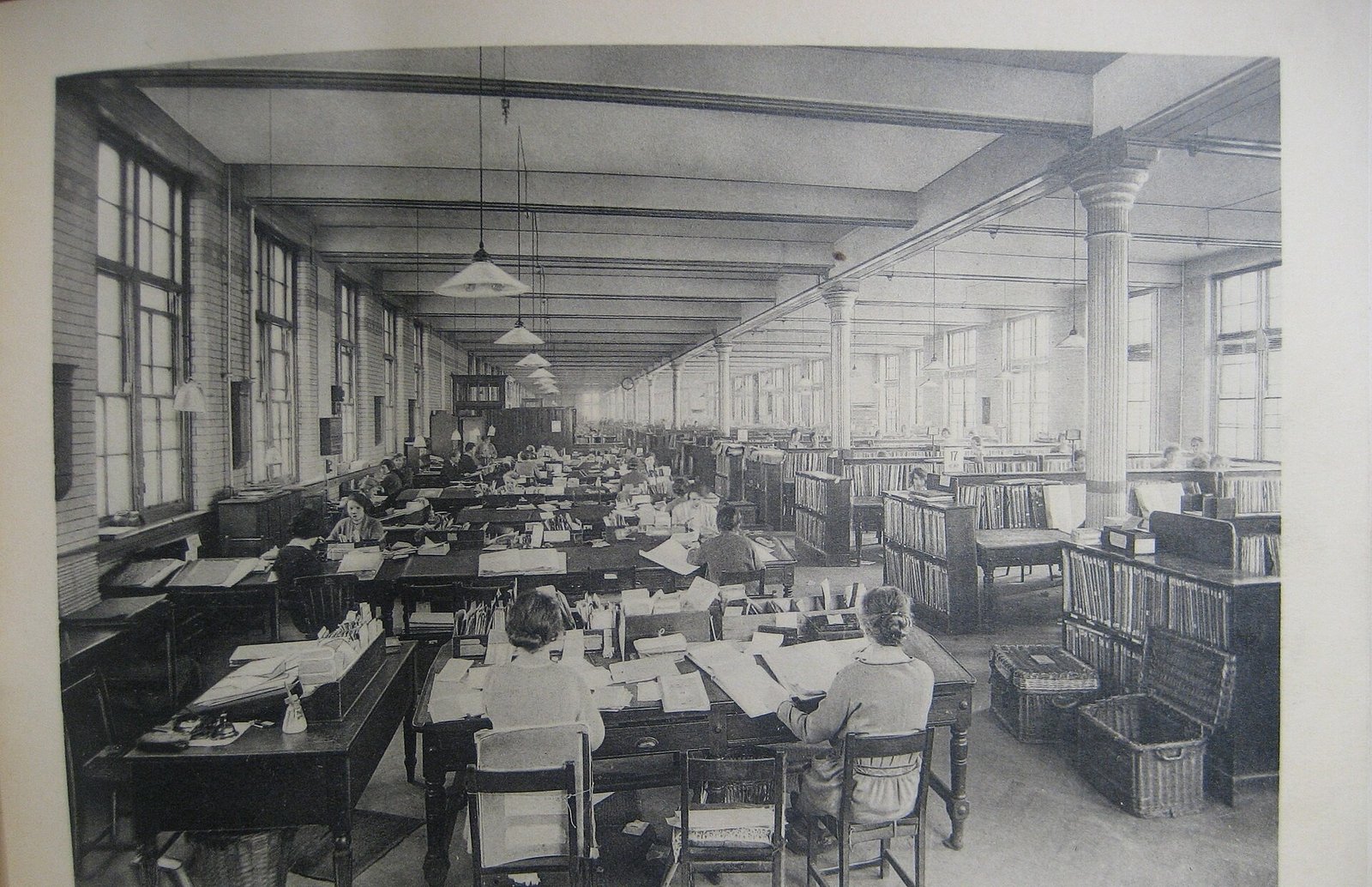 A ledger room at the Post Office Savings Bank, Blythe House, London, 1924: rows of clerks at long desks beneath hanging lamps